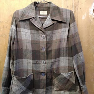 Könnte beinhalten: Eine braun-grau karierte Jacke mit Kragen, Knopfverschluss und zwei Vordertaschen. Die Jacke hängt an einem Metallbügel. Der Stoff hat ein strukturiertes Aussehen.