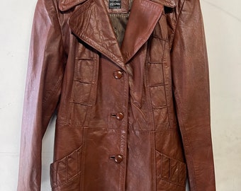 May include: A brown leather jacket with a button-up front and flap pockets. The jacket has a collar and long sleeves.