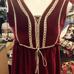 Puede incluir: Un vestido de terciopelo burdeos con ribete de encaje y un lazo en la cintura.