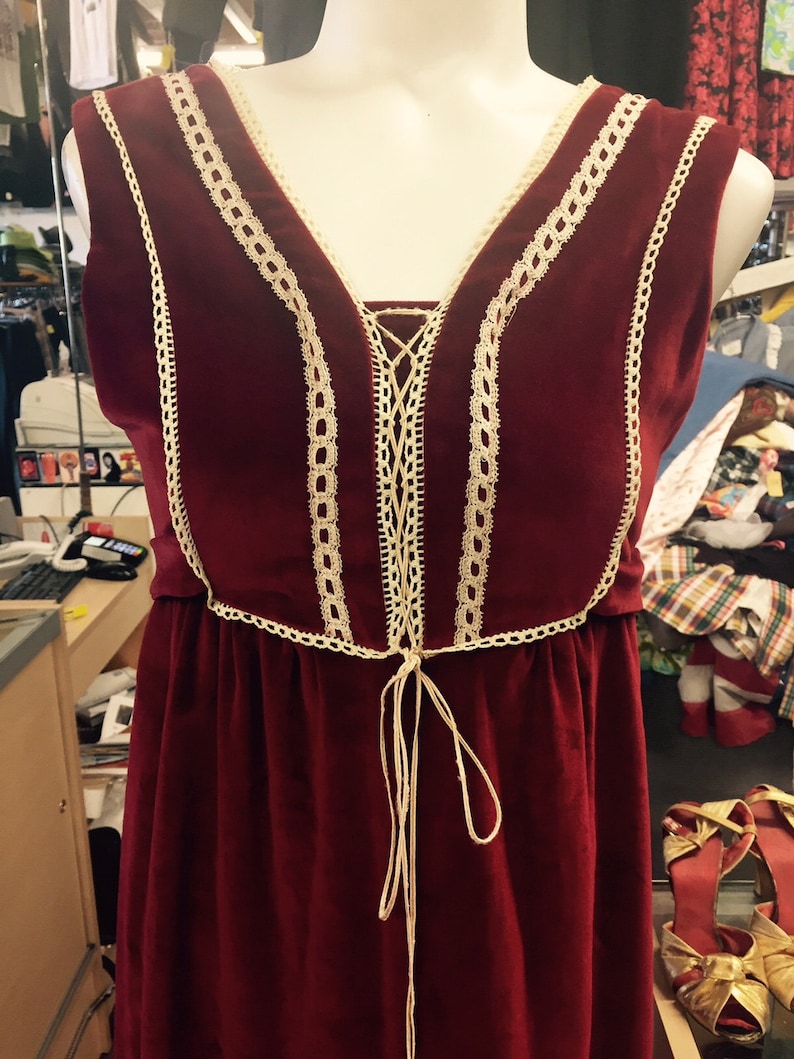 Puede incluir: Un vestido de terciopelo burdeos con ribete de encaje y un lazo en la cintura.