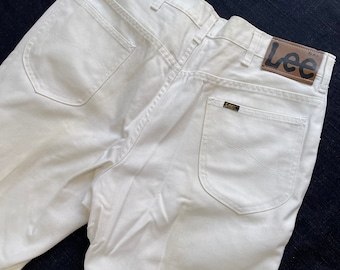 May include: White denim jeans with a brown Lee logo patch on the back right pocket. The jeans have a classic five-pocket style.