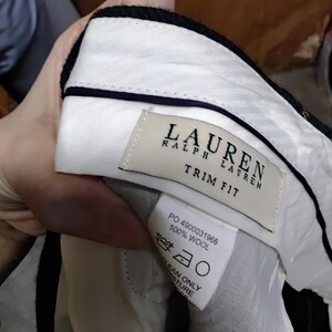 May include: Close-up of the interior of a pair of black wool trousers. The white lining is visible, along with a label that reads "LAUREN RALPH LAUREN TRIM FIT" and a care label. The trousers are made of 100% wool.