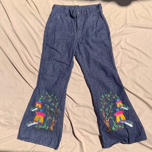Könnte beinhalten: Blaue Jeans mit Glockenbeinen und gestickten Bäumen und Häusern am unteren Ende der Beine.