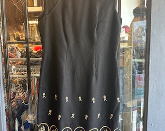 May include: A black sleeveless dress with a mandarin collar and a gold and white embroidered design around the hem.