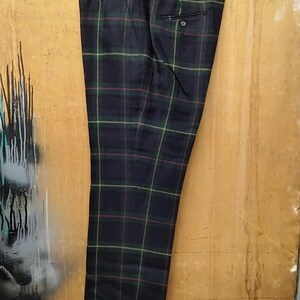May include: Dark navy plaid trousers with green, red, and yellow accents, hanging from a black hanger. The pants feature a buttoned back pocket and a classic tailored design. The plaid pattern is a traditional style.