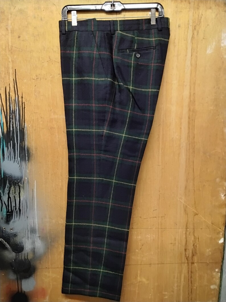 May include: Dark navy plaid trousers with green, red, and yellow accents, hanging from a black hanger. The pants feature a buttoned back pocket and a classic tailored design. The plaid pattern is a traditional style.