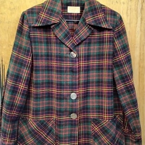 May include: A vintage plaid blazer in shades of green, red, yellow, and purple. The jacket features a classic collar, three large buttons, and two front pockets. The fabric has a traditional tartan pattern.
