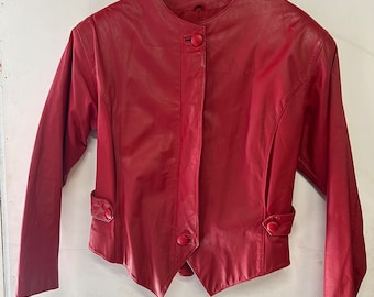 May include: A red leather jacket with a stand-up collar and button fastening. The jacket has a fitted silhouette and a pointed hem.