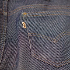 May include: Close-up of the back pocket of a pair of blue denim jeans. The pocket has a brown leather patch with the word "Levi's" printed on it.