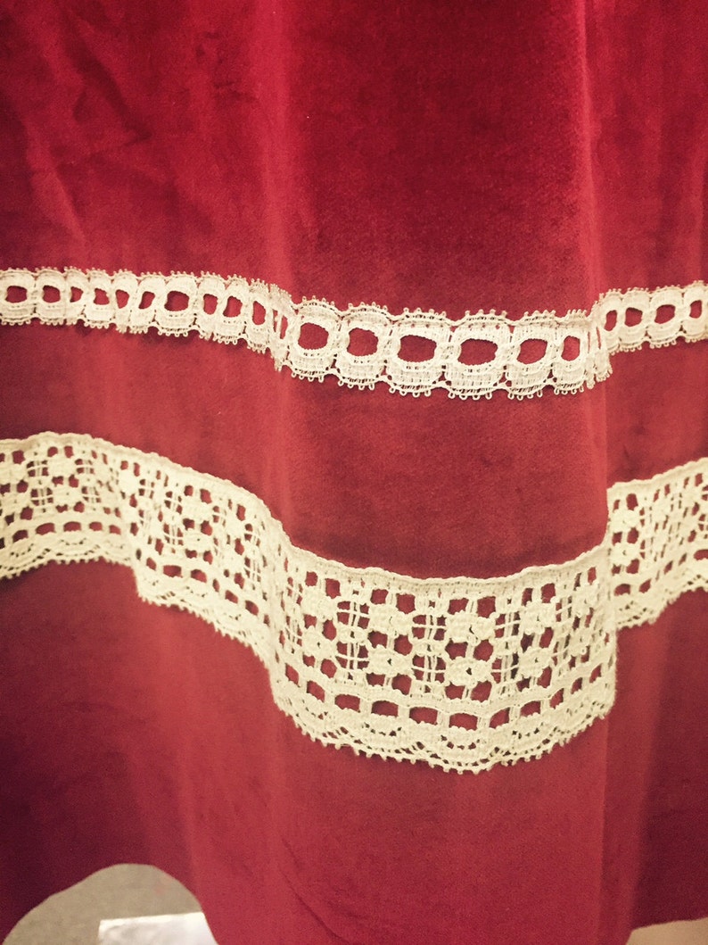Puede incluir: Tela de terciopelo rojo con dos filas de encaje blanco. El encaje es un patr&oacute;n delicado con peque&ntilde;os c&iacute;rculos y cuadrados.