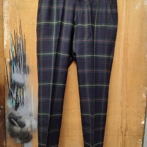 May include: Dark navy plaid trousers with green, red, and yellow accents, hanging on a black hanger. The pants have a classic fit and feature a button closure and belt loops. The fabric appears to be a woven material.