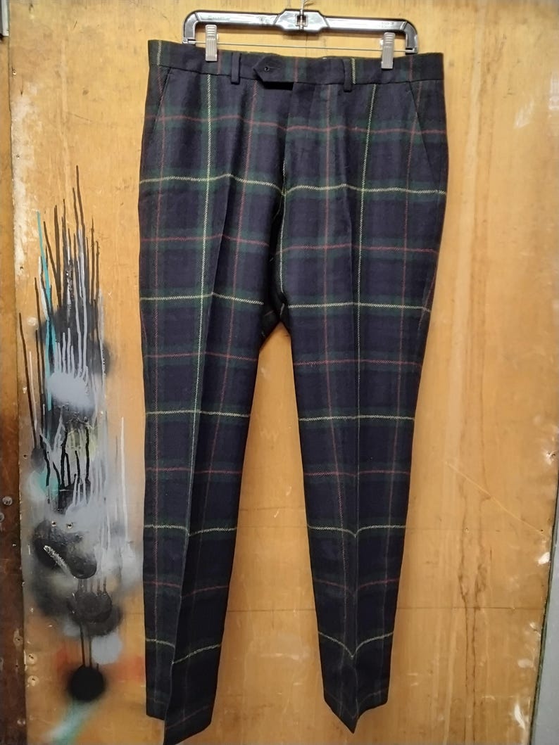 May include: Dark navy plaid trousers with green, red, and yellow accents, hanging on a black hanger. The pants have a classic fit and feature a button closure and belt loops. The fabric appears to be a woven material.