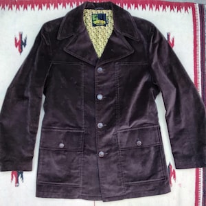May include: A dark brown corduroy jacket with a notched collar, four front buttons, and two front pockets. The jacket has a yellow and green patterned lining and is displayed on a patterned textile.