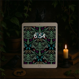 May include: A digital tablet shows a black background with a repeating pattern of green moths, mushrooms, and crescent moons. The time 6:54 is displayed. A lit candle, books, and decorative objects are in the background.