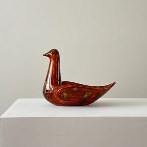 May include: A ceramic bird-shaped bowl with a red and brown glaze and green accents. The bowl is sitting on a white surface.