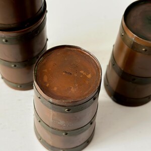 May include: Three antique copper-toned barrel-shaped containers with dark metal bands and rivets. The containers have a rich, warm brown colour and a vintage aesthetic. The tops are flat and circular.