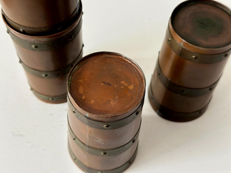 May include: Three antique copper-toned barrel-shaped containers with dark metal bands and rivets. The containers have a rich, warm brown colour and a vintage aesthetic. The tops are flat and circular.