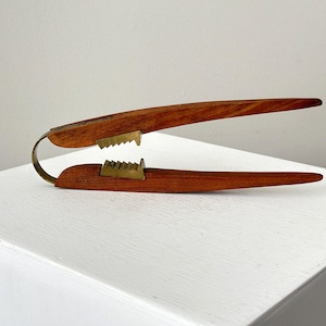 May include: A wooden nutcracker with brass teeth. The nutcracker is made of dark wood and has a simple design.