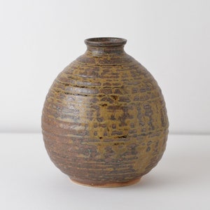 May include: A brown ceramic vase with a textured surface. The vase has a rounded body and a narrow opening.