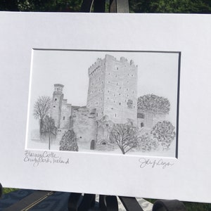 May include: A black and white pencil drawing of Blarney Castle in County Cork, Ireland. The drawing shows the castle's tall tower and surrounding buildings. The artist's signature, John Regan, is in the bottom right corner.