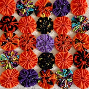 May include: A quilt block pattern with 25 fabric squares. The squares are in a variety of colors, including orange, purple, black, white, and green. Each square has a different design, including polka dots, stripes, and floral patterns.