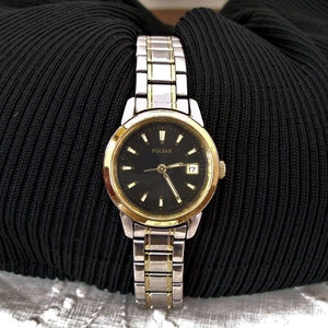 May include: A two-tone silver and gold women's wristwatch with a black face and a date window. The watch face has the word "PULSAR" printed on it.