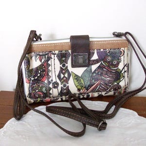 May include: A rectangular crossbody bag with a cream-colored base featuring a multi-colored graphic print of stylized birds and geometric patterns. The bag includes a dark brown faux leather strap, a matching brown flap closure, and a silver metal clasp.