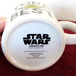 K&ouml;nnte beinhalten: Wei&szlig;e Keramiktasse mit dem Star Wars-Logo und dem Text "TODAY IS THE BEST DAY". Die Tasse hat einen abgerundeten Henkel und ein Charakterdesign. Der Boden der Tasse zeigt das Star Wars-Logo und die Website.