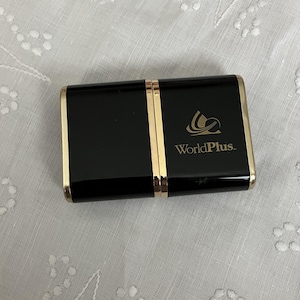 May include: A rectangular black case with gold trim and a gold vertical stripe down the center. The text "WorldPlus" is printed in gold on the right side of the case, along with a gold logo.