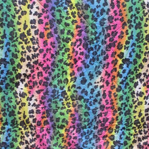 May include: A vibrant textile featuring a rainbow-colored background with vertical stripes. The design is overlaid with a pattern of black leopard spots, creating a bold and colorful animal print. The fabric has a slightly wrinkled texture.
