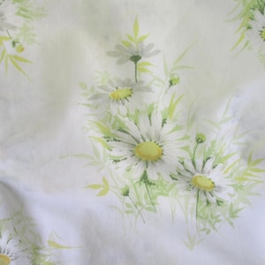 Puede incluir: Tela blanca con un estampado floral de margaritas. Las margaritas tienen pétalos blancos y centros amarillos, con hojas y tallos verdes. La tela tiene un aspecto suave y ligeramente arrugado.