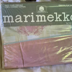 Puede incluir: Una sábana plana completa en un paquete de plástico. La sábana es rosa, blanca y azul claro con un estampado floral. El paquete dice "marimekko by Dan River" y "EASY-CARE PERCALE 100% COMBED COTTON".