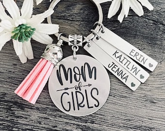 May include: A silver keychain with a pink tassel, a round charm that says "Mom of Girls" with an arrow, and three silver charms with the names "Erin", "Kaitlyn", and "Jenna" engraved on them.