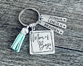 May include: A silver keychain with a turquoise tassel and a square tag that says "Mom of Boys". Three smaller tags with the names "Joshua", "Lincoln", and "Brayden" are attached to the keychain.