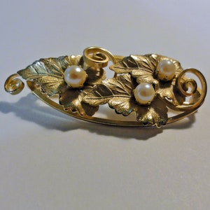 May include: A gold-toned brooch with three faux pearls set in a design of stylized leaves.