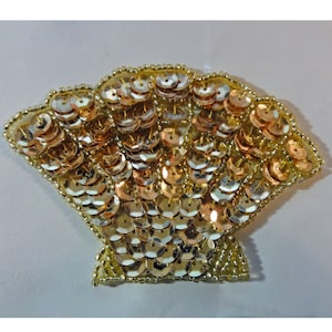 May include: A gold and copper sequined seashell applique. The shell is made of small, round sequins that are sewn together in a fan shape.