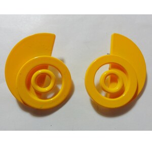 May include: A pair of yellow plastic earrings with a spiral design. The earrings are made of three concentric circles with a crescent shape on the outside.