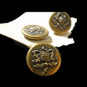 Puede incluir: Tres botones de metal de color dorado con un diseño en relieve de un escudo que presenta una corona y otros elementos decorativos.