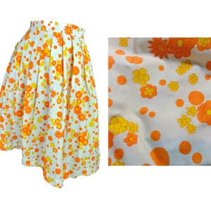 May include: A white skirt with a floral print in orange and yellow. The skirt has a pleated design and a scalloped hem.