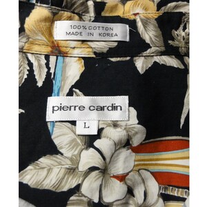 May include: A black button-up shirt with a floral print. The shirt has a white label that says "Pierre Cardin" and a smaller white label that says "100% Cotton Made in Korea". The shirt is size L.