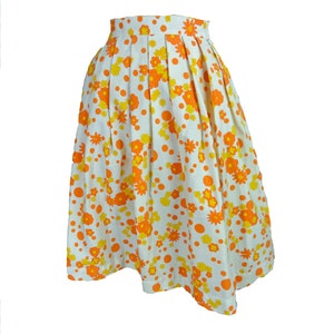 May include: A white skirt with a floral print in orange and yellow. The skirt has a pleated design and a fitted waist.
