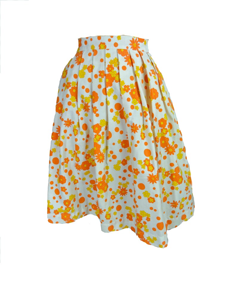 May include: A white skirt with a floral print in orange and yellow. The skirt has a pleated design and a fitted waist.