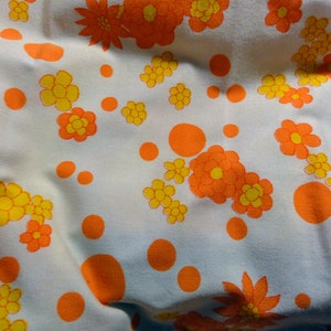 May include: White fabric with a repeating pattern of orange and yellow flowers and orange dots.