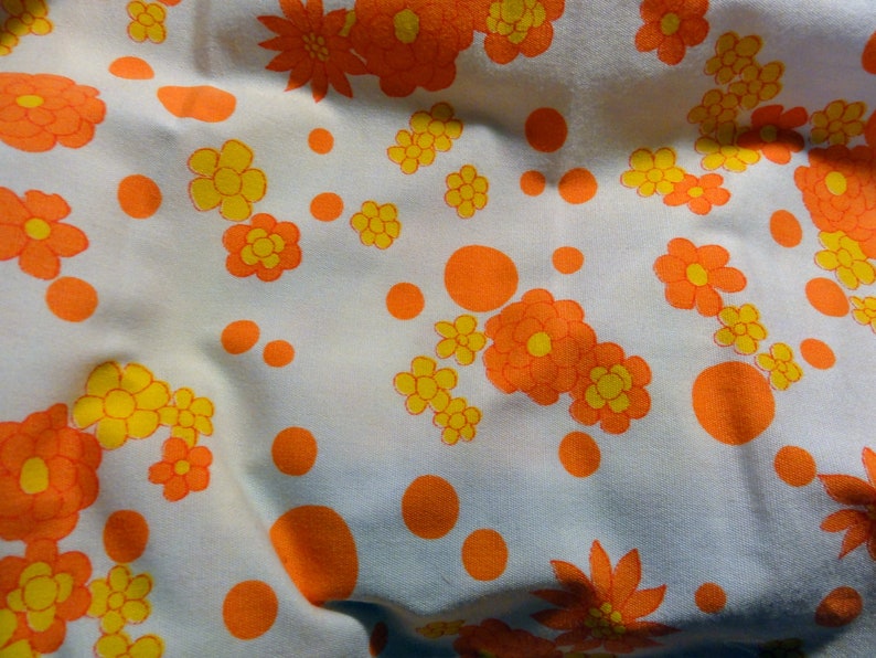 May include: White fabric with a repeating pattern of orange and yellow flowers and orange dots.