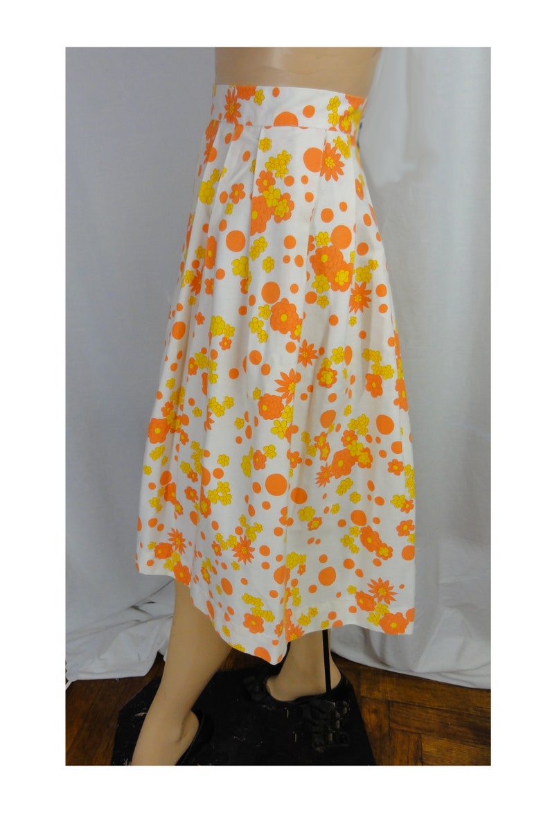May include: A white midi skirt with a floral print featuring orange and yellow flowers and orange polka dots.