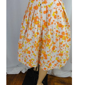 May include: A white skirt with a floral print in orange and yellow. The skirt has a pleated design and a zipper closure in the back.