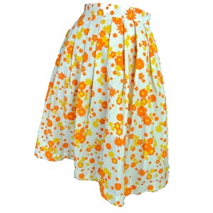 May include: A white skirt with a floral print in orange and yellow. The skirt has a pleated design and a scalloped hem.