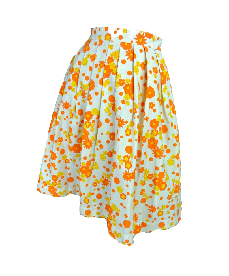 May include: A white skirt with a floral print in orange and yellow. The skirt has a pleated design and a scalloped hem.
