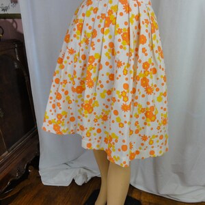May include: A white skirt with a pleated design and a floral print in orange and yellow. The skirt has a fitted waist and a flared hem.