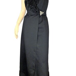 May include: A black sleeveless maxi dress with a ruffled neckline and a wrap-style skirt. The dress has a silver-toned buckle at the waist.